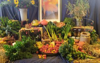 ein Altar-Tisch mit Gemüse, Obst und Bild im Hintergrund
