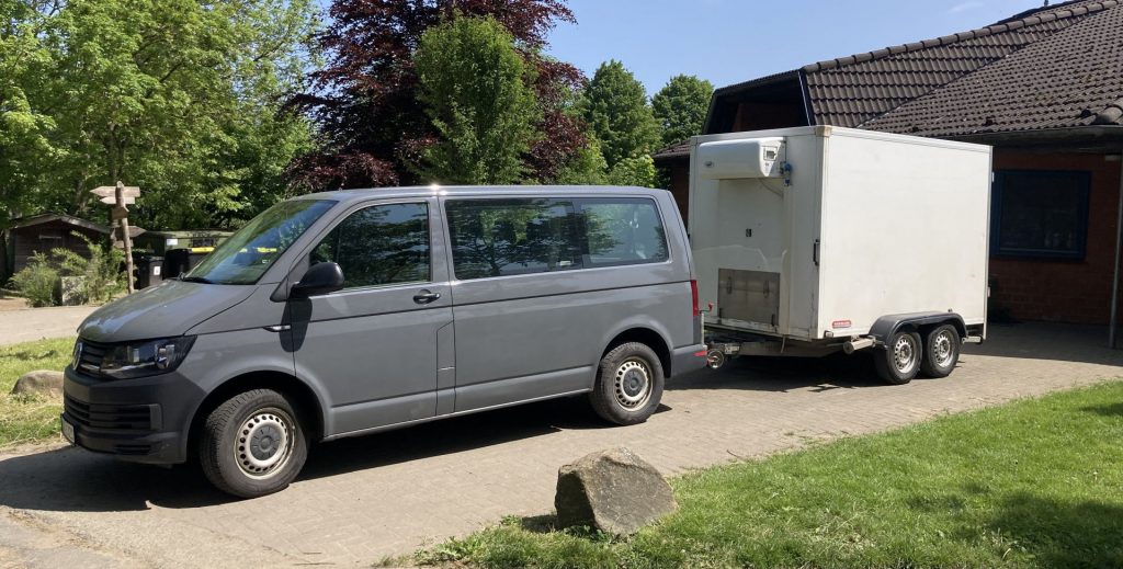 ein kleiner Van mit Anhänger vor einem Haus geparkt