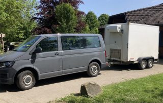 ein kleiner Van mit Anhänger vor einem Haus geparkt