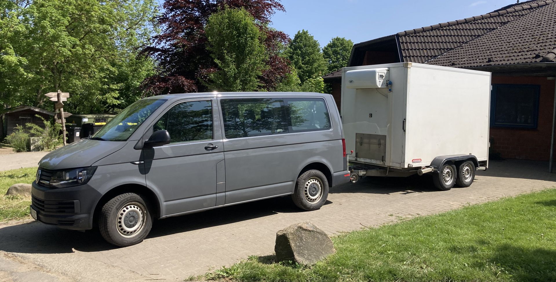 ein kleiner Van mit Anhänger vor einem Haus geparkt